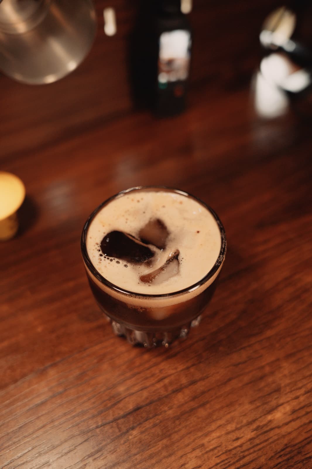 Close-up of iced coffee with foam and a large ice cube